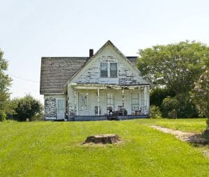 A deteriorated house stands alone in an open field.