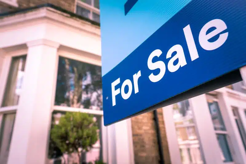 A house has a “for sale” sign in its fence. 