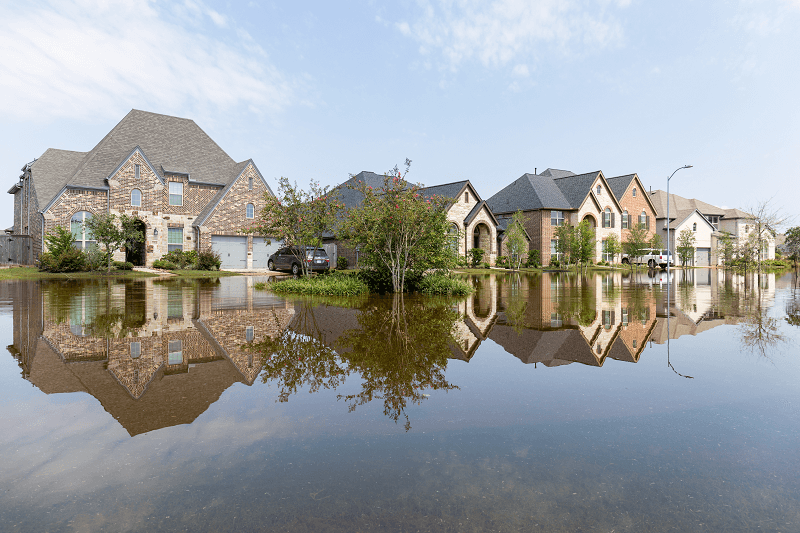 A house for sale with storm damage in a flooded street