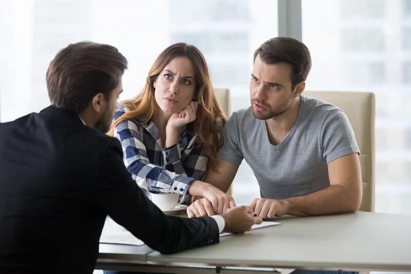 A young couple of homeowners argue with their lender about lender required repairs on their property